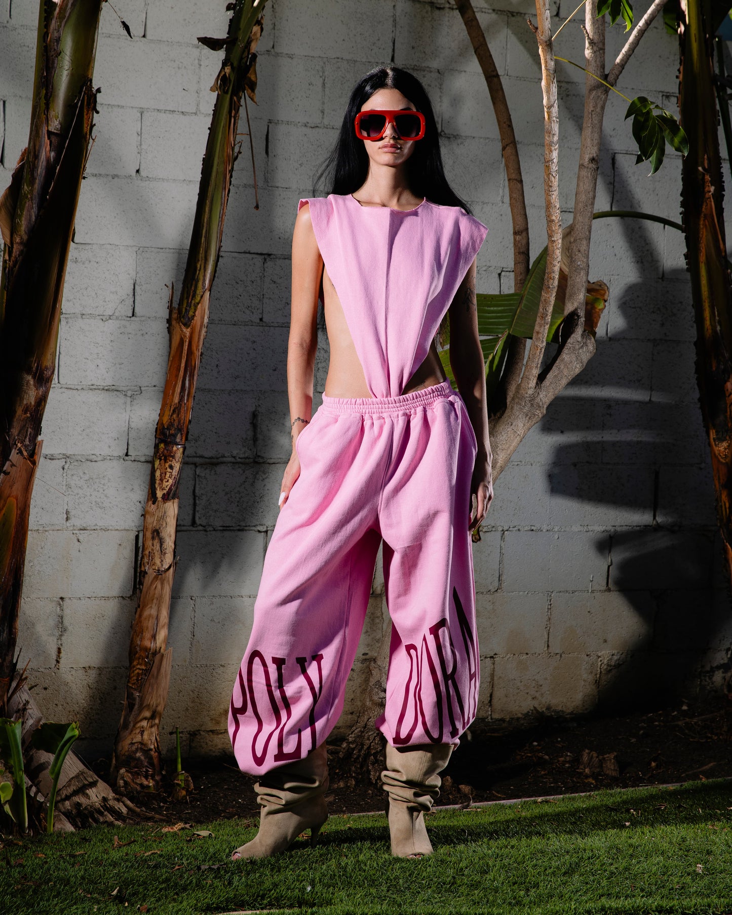Person wearing a pink outfit with 'HOLY' text, standing outdoors against a concrete wall.